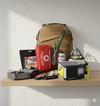 Sfeerbeeld luxe noodpakket Paraat Premium: rugzak, EHBO-set, waterfilter, noodradio met solar, multitool, hoofdlamp, powerbank en noodrantsoen op plank.